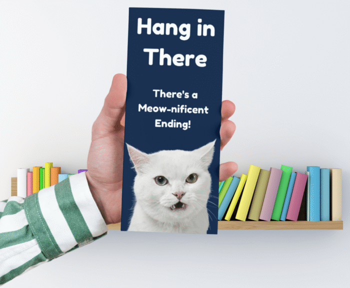Printable Hang in There Cat Bookmark held in hand with bookshelf background.