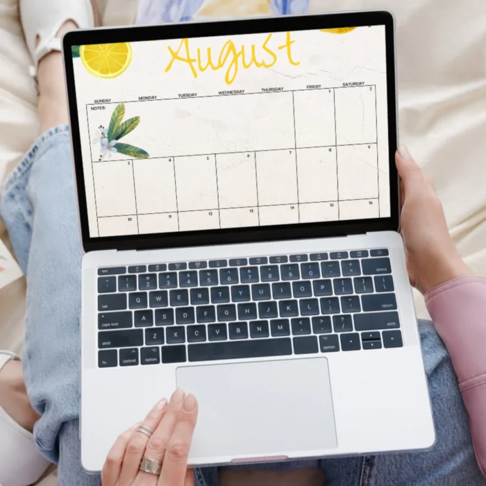 Woman holding laptop with lemon August 2025 calendar displayed.